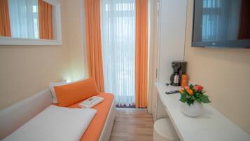 Ein Hotelzimmer mit einem Bett, einem kleinen Tisch mit Kaffeemaschine, einem Fernseher und einer Vase mit Blumen.
