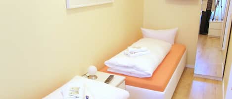 Quarto de hotel com duas camas de solteiro, uma mesa pequena com abajur, televisão na parede e um quadro de um edifício.