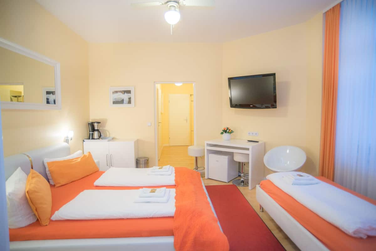 Habitación de hotel con dos camas, un escritorio, un televisor y un baño visible a través de una puerta abierta.