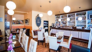 Un restaurant doté d’un bar, de chaises blanches, de tables en bois et de luminaires suspendus.