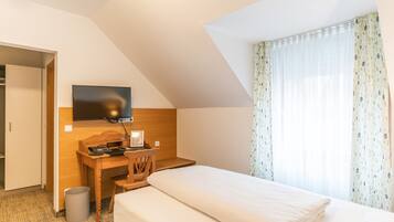 Una camera d'albergo con un letto, una scrivania con una sedia, una televisione a parete e una finestra con tende.