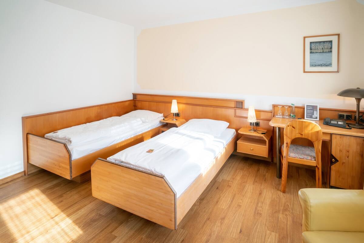 A room with two wooden beds, a desk, a chair, and a nightstand with lamps.