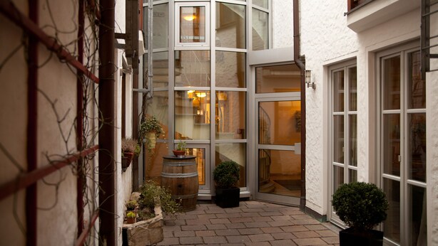 A narrow courtyard with a glass door entrance, potted plants, and a wooden barrel. - Altstadthotel Grauer Wolf (Erlangen)