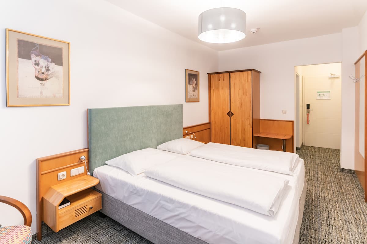 A hotel room with a bed, a wooden nightstand, a wardrobe, and a framed picture on the wall.