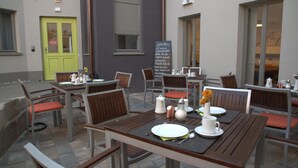 An outdoor cafe with tables and chairs, a chalkboard menu, and a green door. - Altstadthotel Grauer Wolf (Erlangen)