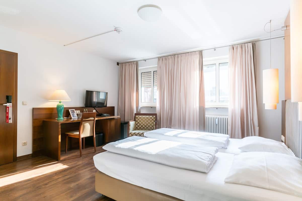 A hotel room with a bed, desk, chair, TV, and curtains.