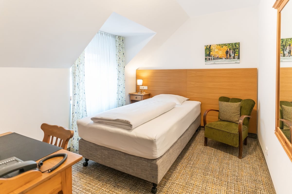 A hotel room with a bed, a desk with a telephone, a chair, a nightstand with a lamp, and a painting on the wall.