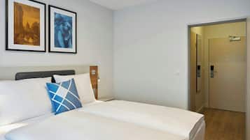 Ein Hotelzimmer mit einem Bett, zwei gerahmten Bildern an der Wand und einer Tür zu einem weiteren Raum.