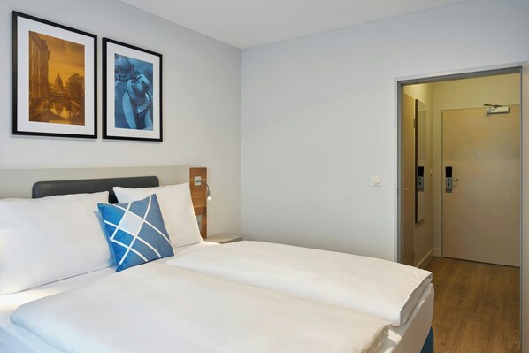Una habitación de hotel con una cama, dos cuadros en la pared y una puerta que da a otra habitación.