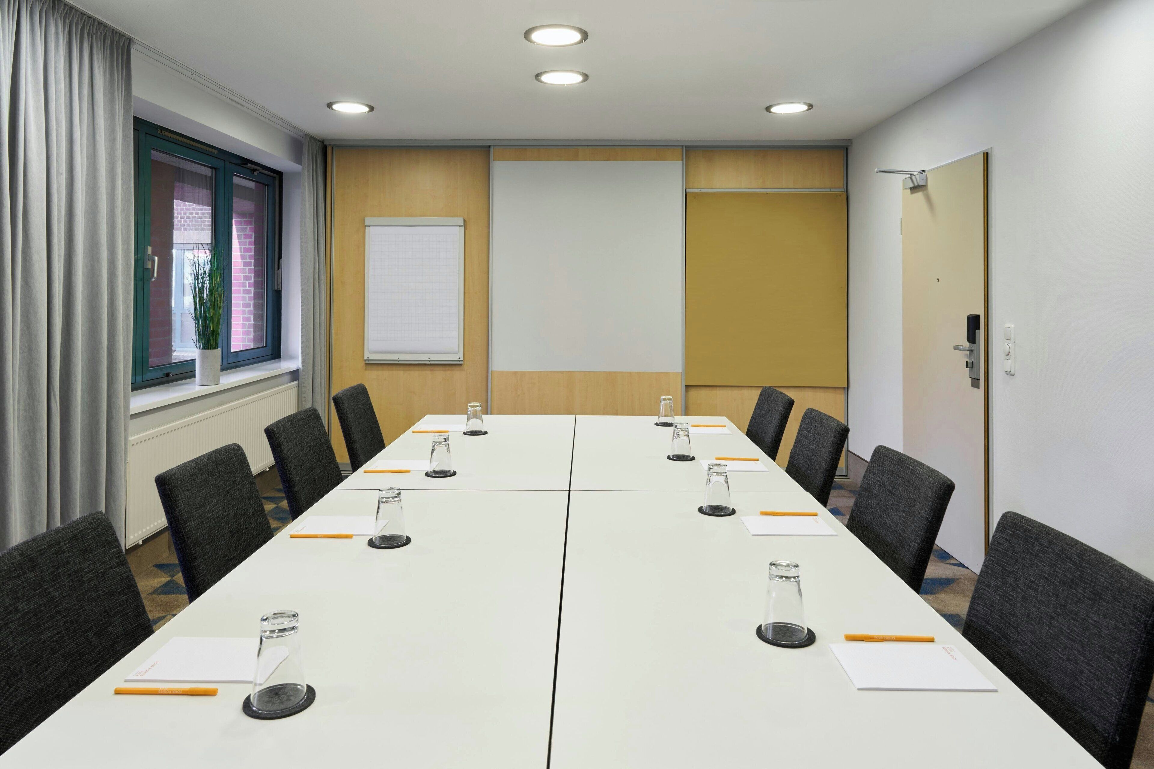 A conference room with a long table, chairs, a projector screen, and a whiteboard.