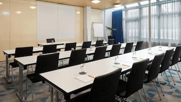 A conference room with long tables, chairs, a whiteboard, and a projector screen.