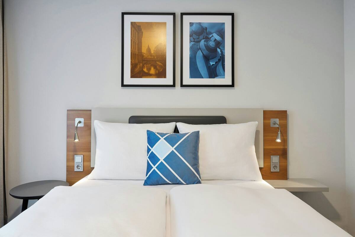 A double bed with white linens, a blue and white pillow, and two framed pictures above it.
