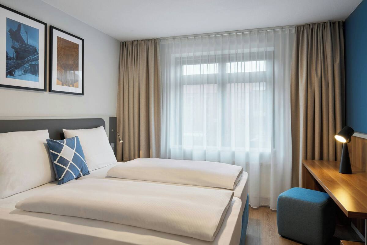 A hotel room with a bed, a desk, and a window with curtains.