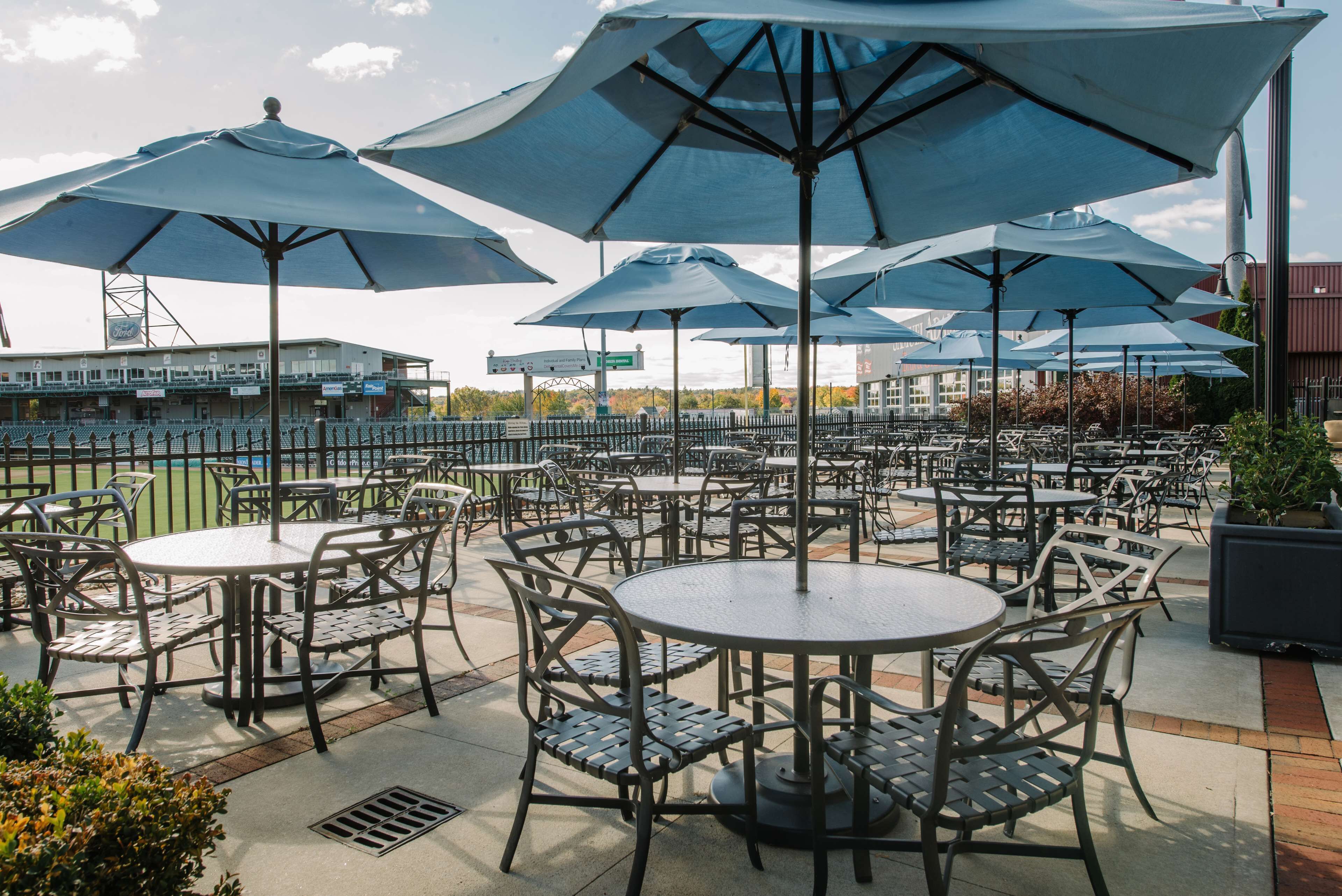 Un espace extérieur aménagé en terrasse, avec des tables et des chaises rondes, protégé par de grands parasols, et offrant une vue sur un bâtiment en arrière-plan.