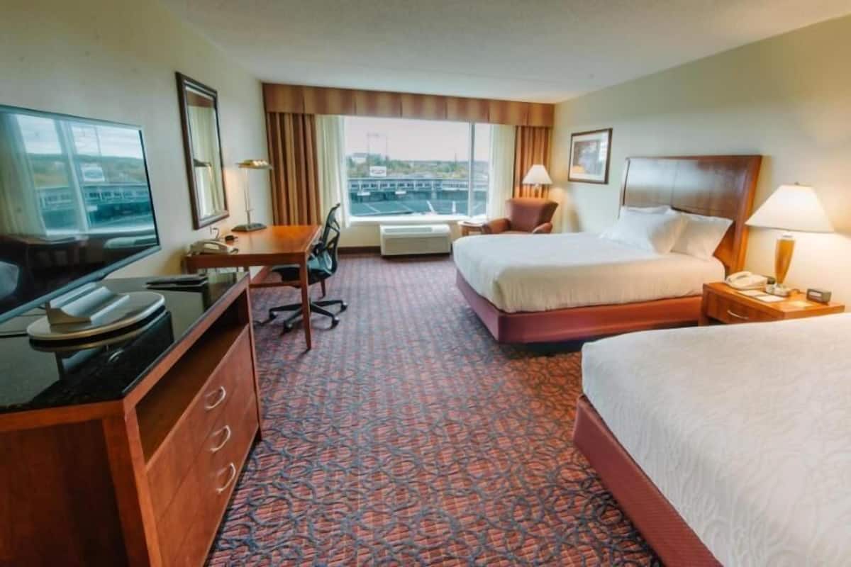 A hotel room with a bed, desk, chair, television, and a view of the city.
