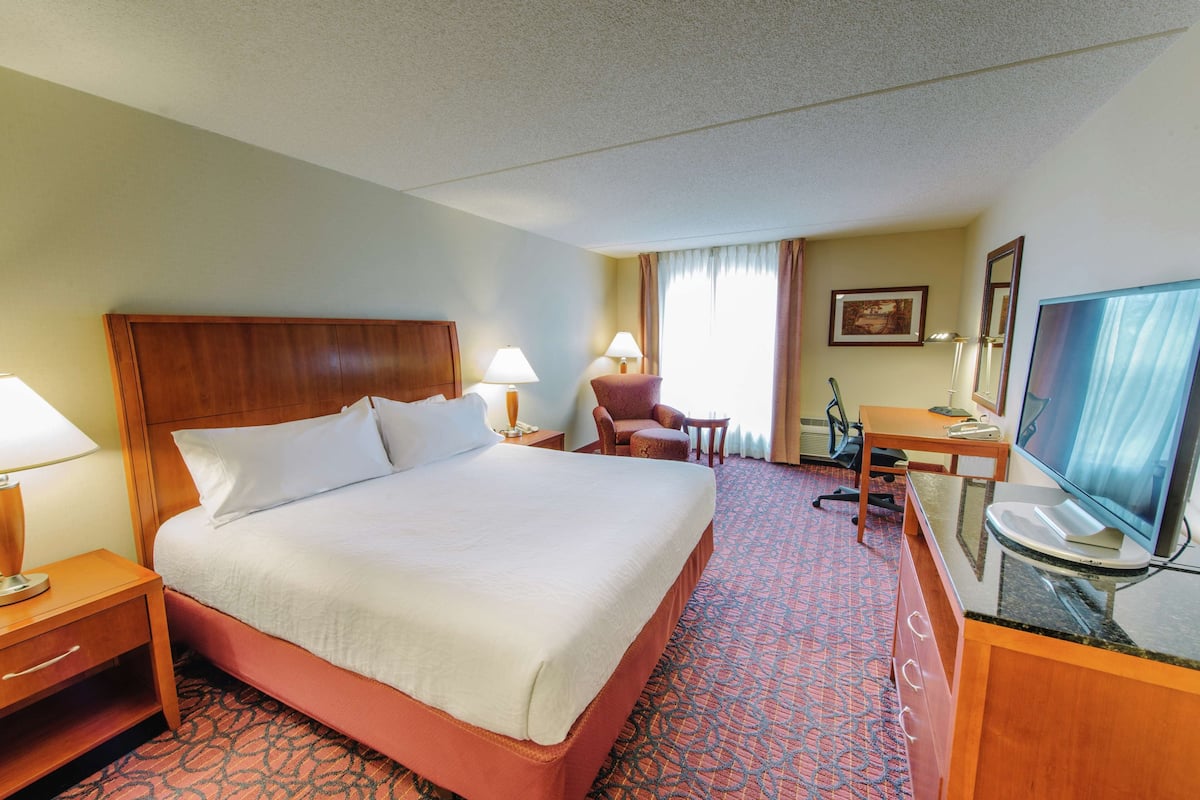 A hotel room with a large bed, a desk with a computer, a chair, and a television.