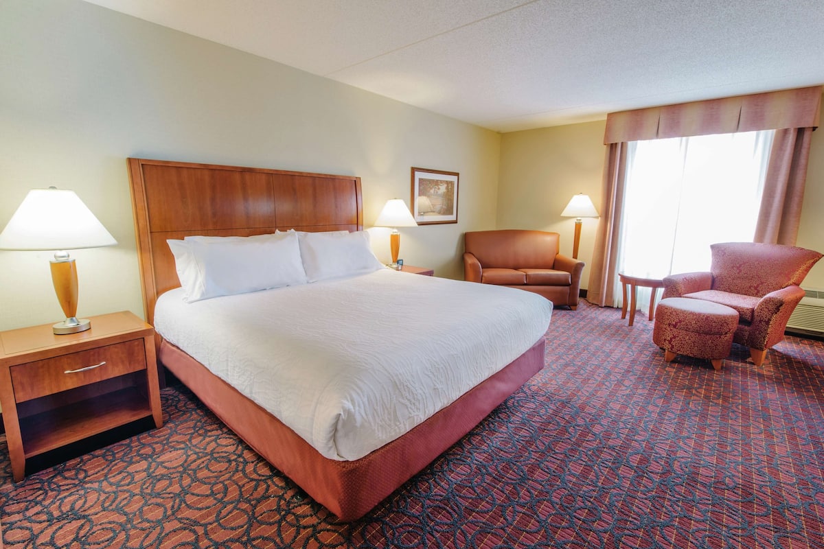 A hotel room with a large bed, two chairs, a nightstand, and a lamp.