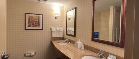 A hotel bathroom with two sinks, a large mirror, a framed picture on the wall, and a toilet.