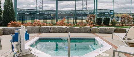 A pool area with a hot tub, lounge chairs, and a view of a baseball stadium in the background.