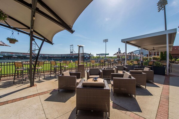 Un espace extérieur aménagé avec des meubles en osier et des parasols, donnant sur un terrain de baseball.