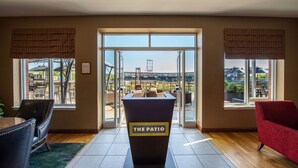 A room with a large window, a podium labeled "The Patio," and a view of an outdoor seating area. - Hilton Garden Inn Manchester Downtown (Manchester)