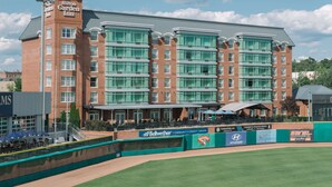 A Hilton Garden Inn with a clock tower, large windows, and a baseball field in front. - Hilton Garden Inn Manchester Downtown (Manchester)