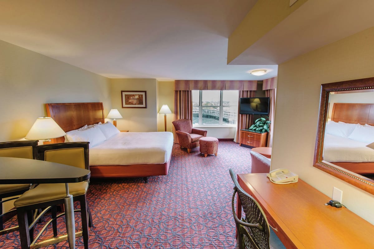 A hotel room with a large bed, a desk with a telephone, a chair, a small table, and a TV.