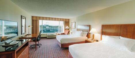 A hotel room with two beds, a desk, a chair, a TV, and a window with a city view.