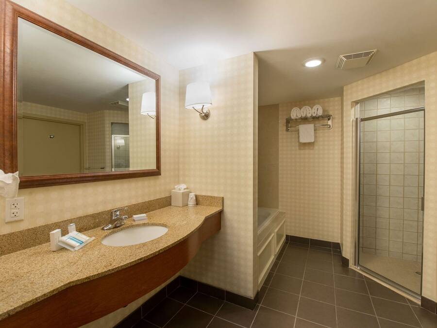A hotel bathroom with a large mirror, a sink, a shower, and a towel rack.