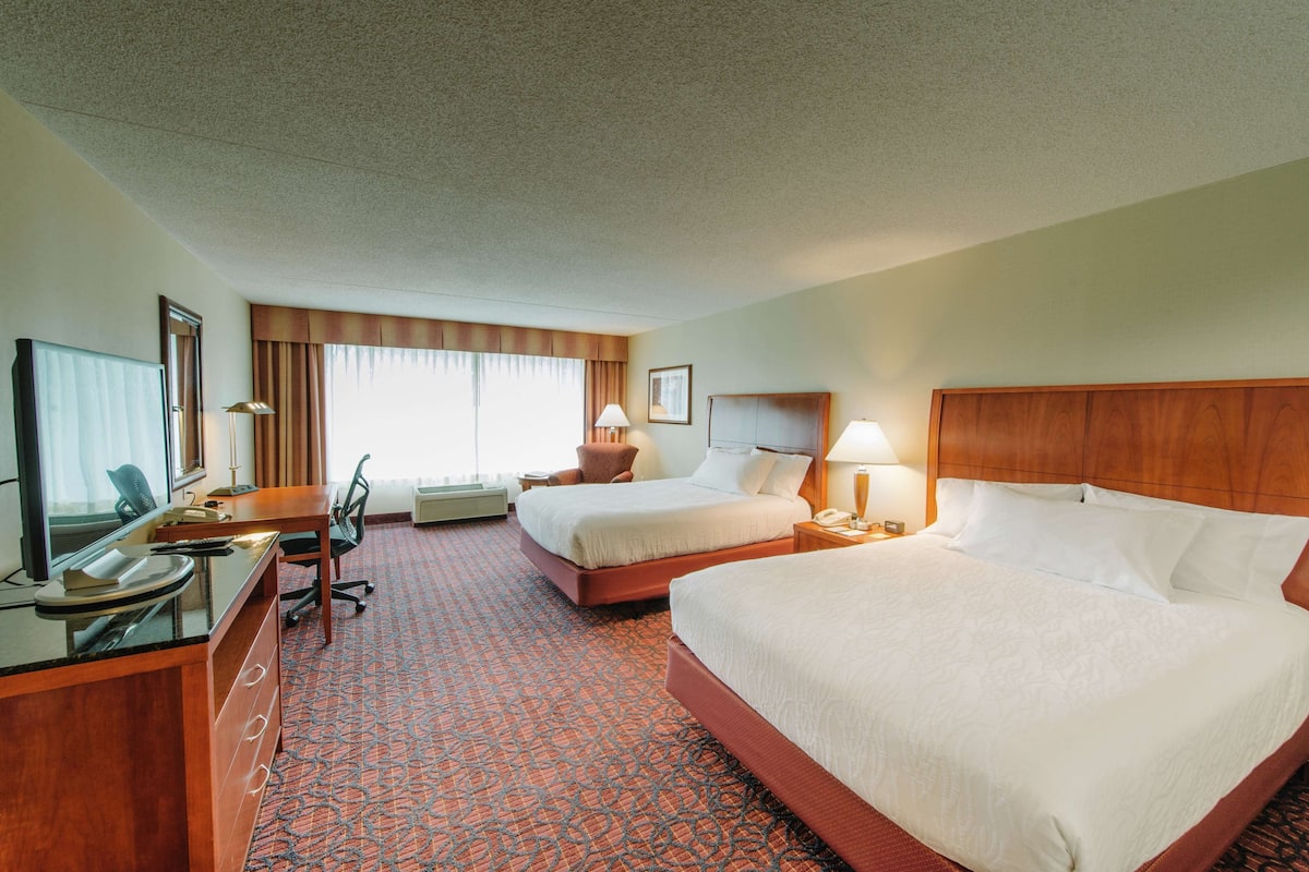 A hotel room with two beds, a desk with a computer, and a chair.