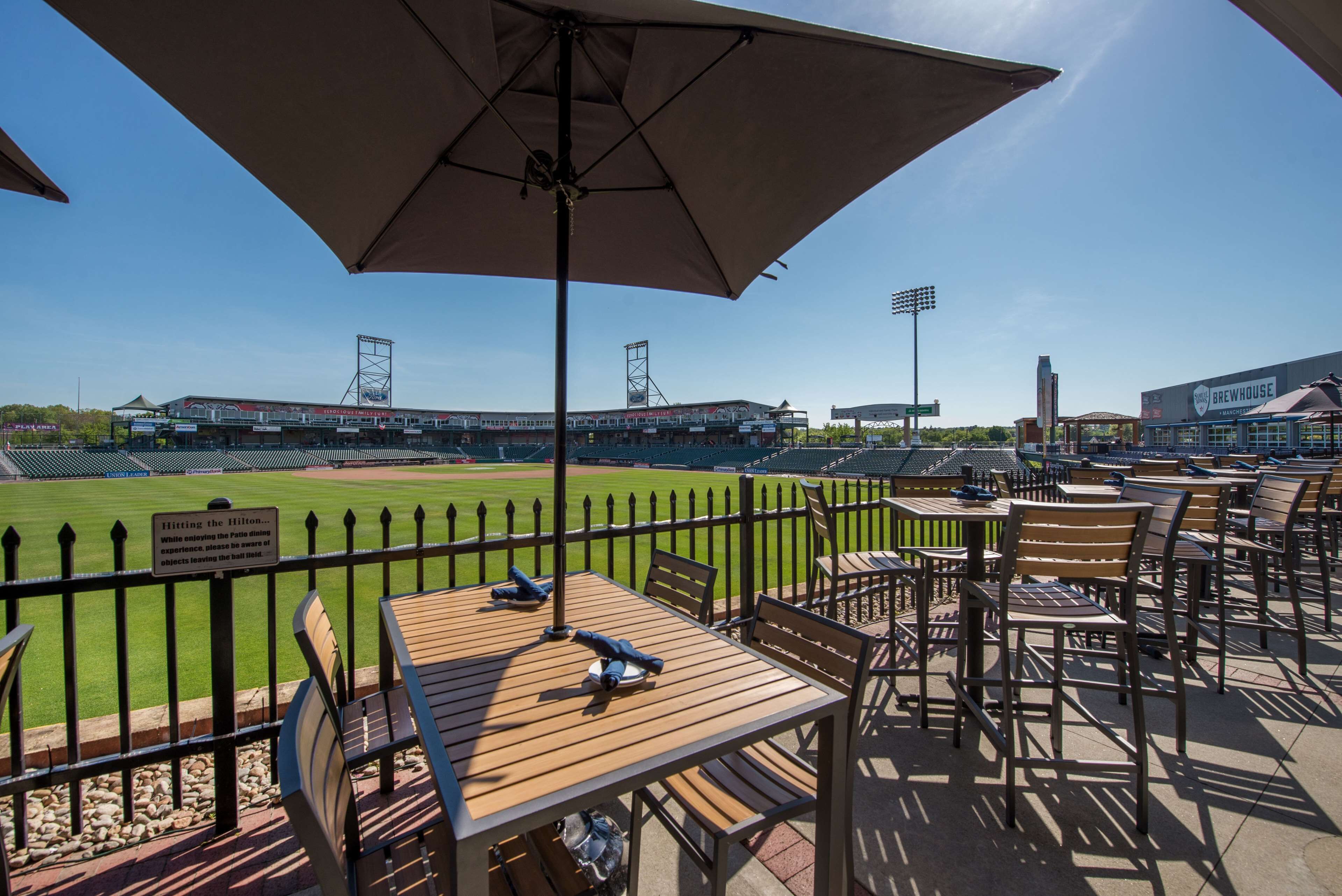 A patio area with tables and chairs, overlooking a baseball field.