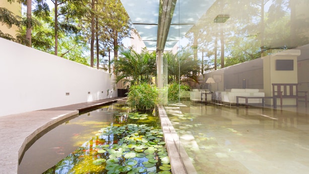 Un moderno atrio interior con piso reflectante, una fuente central con lirios y un techo de vidrio que permite la luz natural.