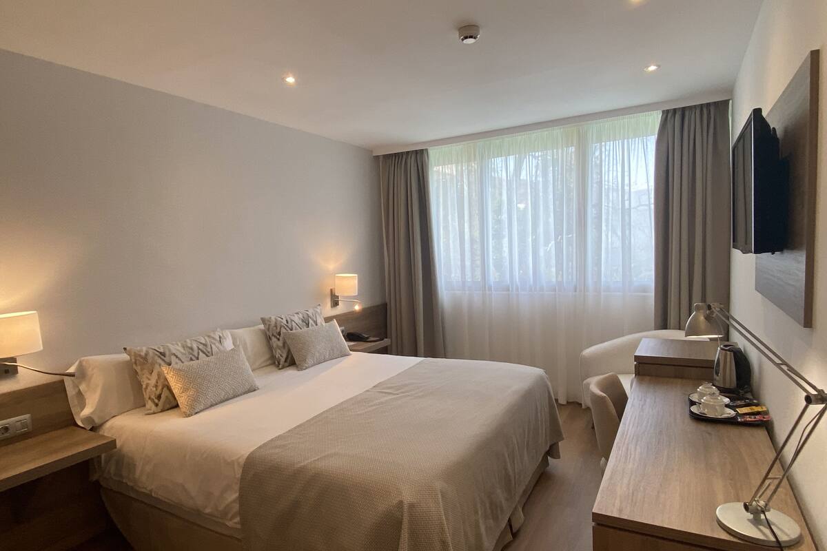 A hotel room with a large bed, bedside tables with lamps, a desk with a chair, and a TV mounted on the wall.