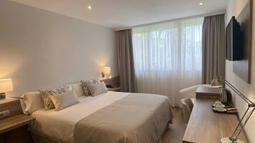Habitación de hotel con una cama grande, mesitas de noche con lámparas, un escritorio con una silla y un televisor fijado en la pared.