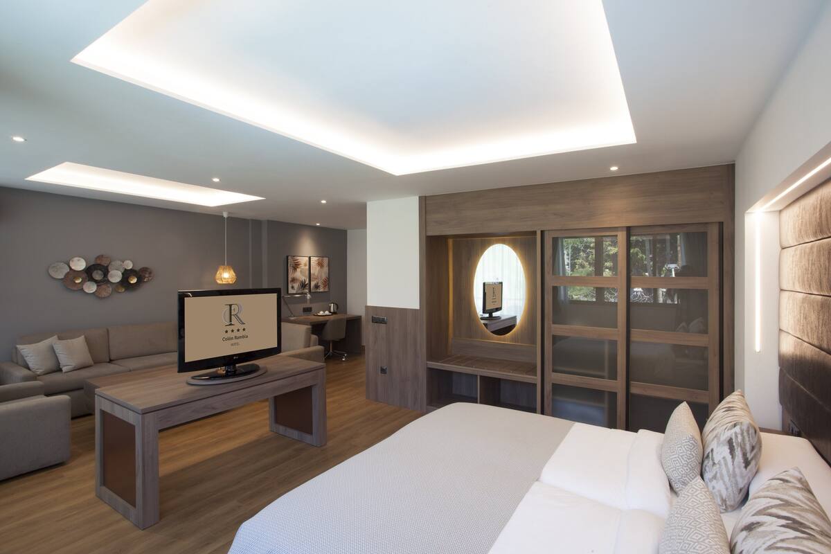 A modern hotel room with a large bed, a desk, a sofa, and a TV.