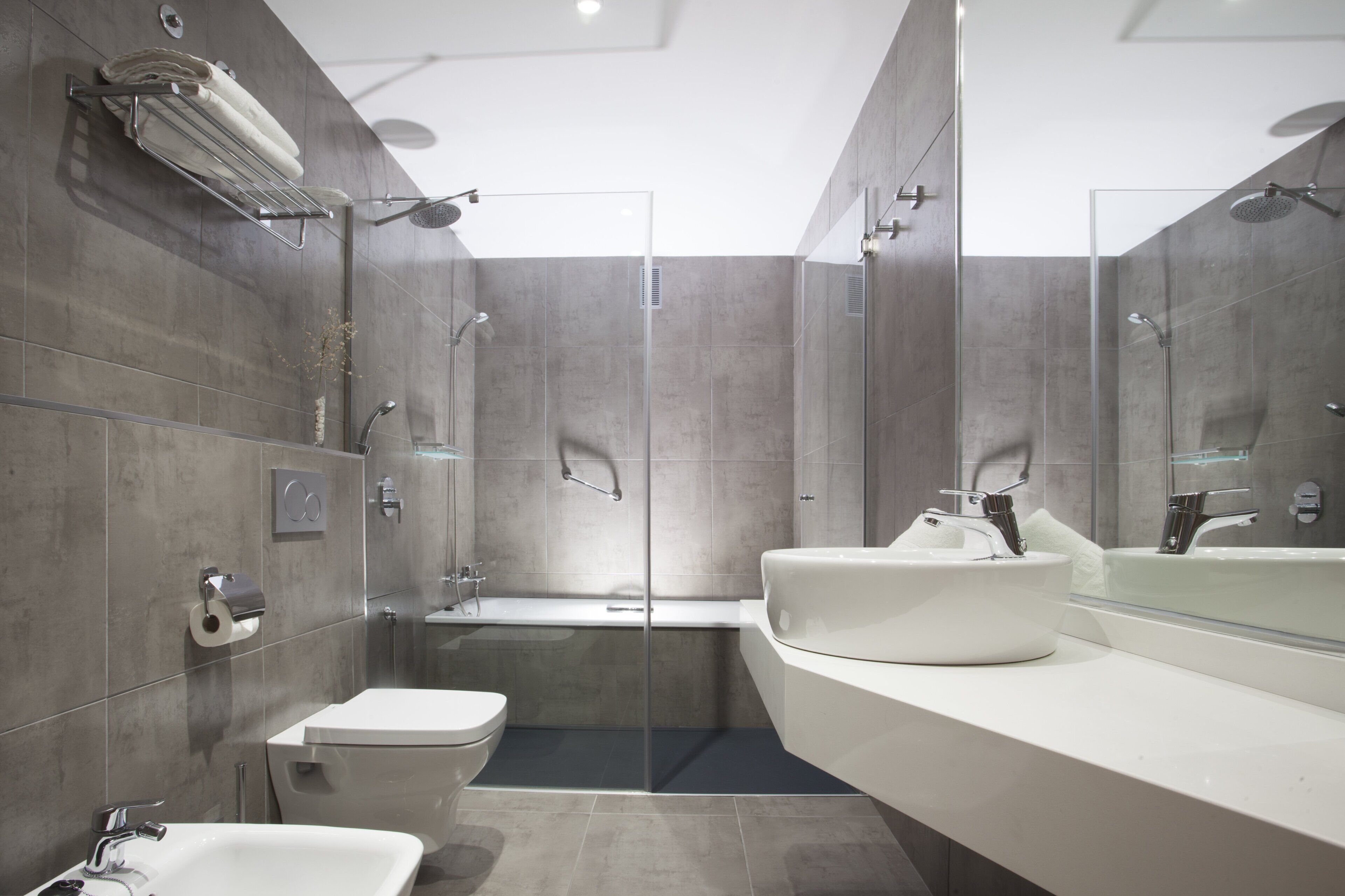 A modern bathroom with a glass-enclosed shower, a bathtub, a toilet, and a large vanity with a mirror.