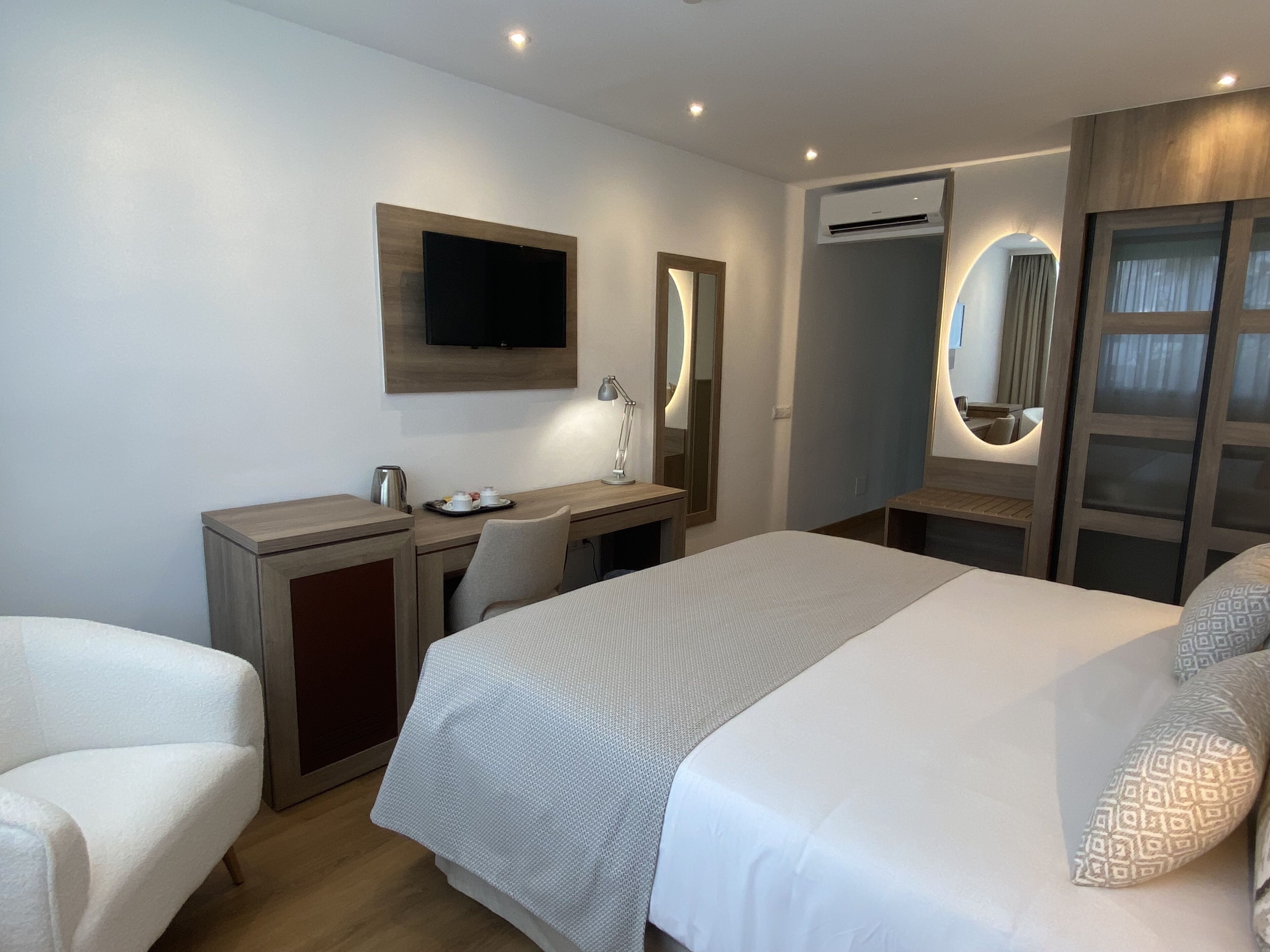 Habitación de hotel con cama, escritorio, silla, televisor y unidad de aire acondicionado.