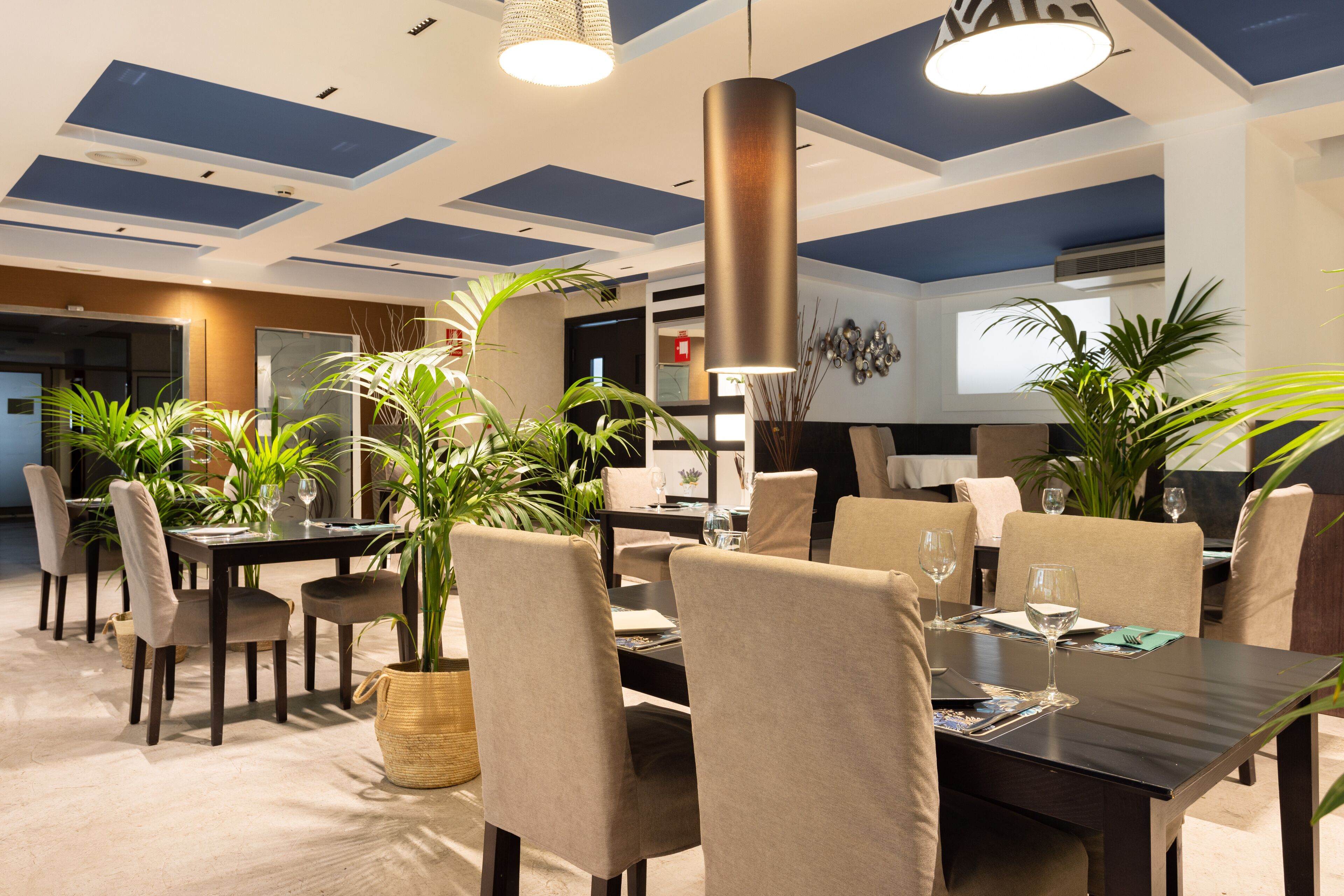 Un comedor moderno con una mesa de madera oscura, sillas tapizadas en tono beige y plantas en macetas.