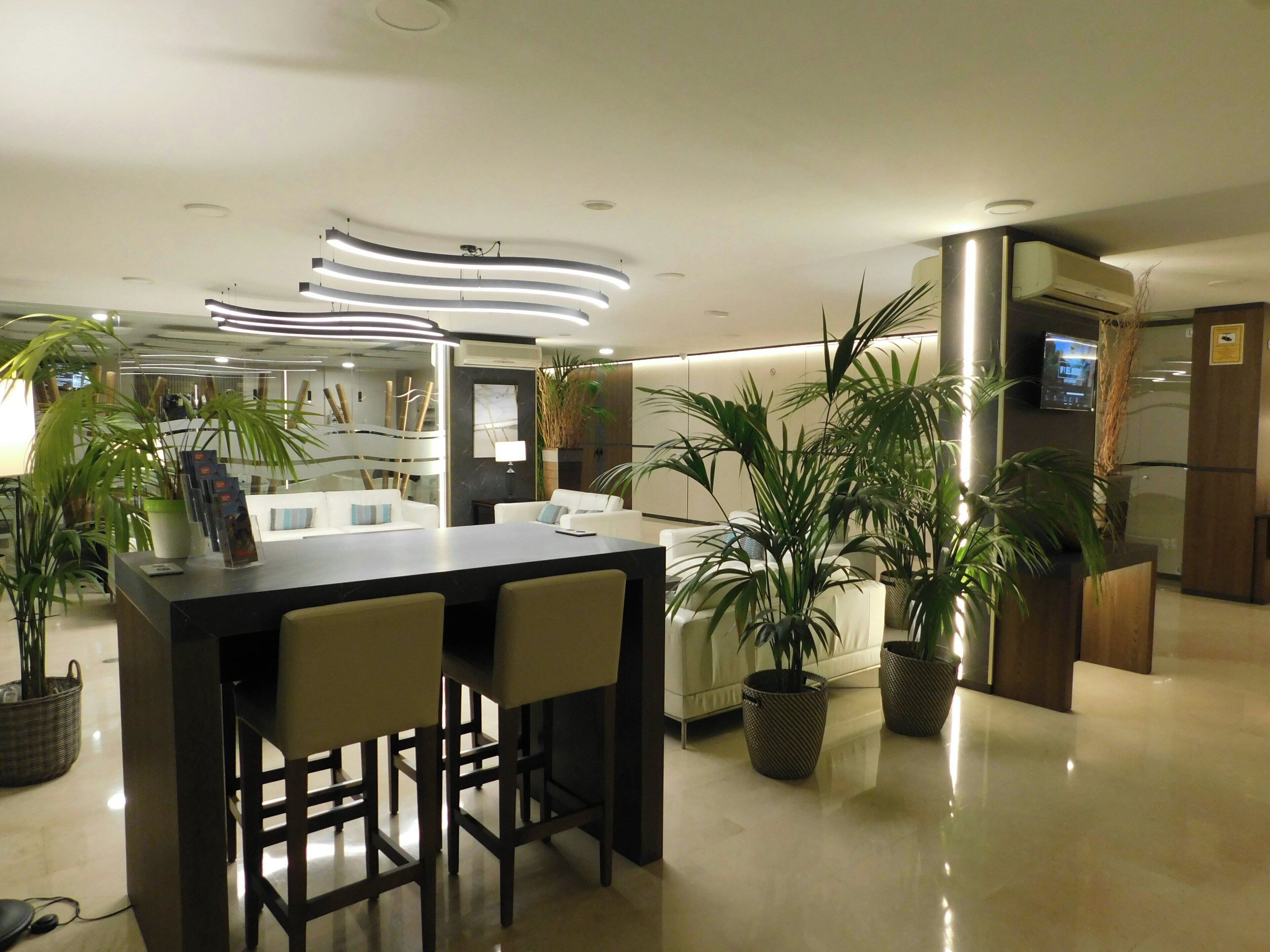 Un moderno vestíbulo de hotel con mostrador de recepción, zona de estar y plantas en macetas.