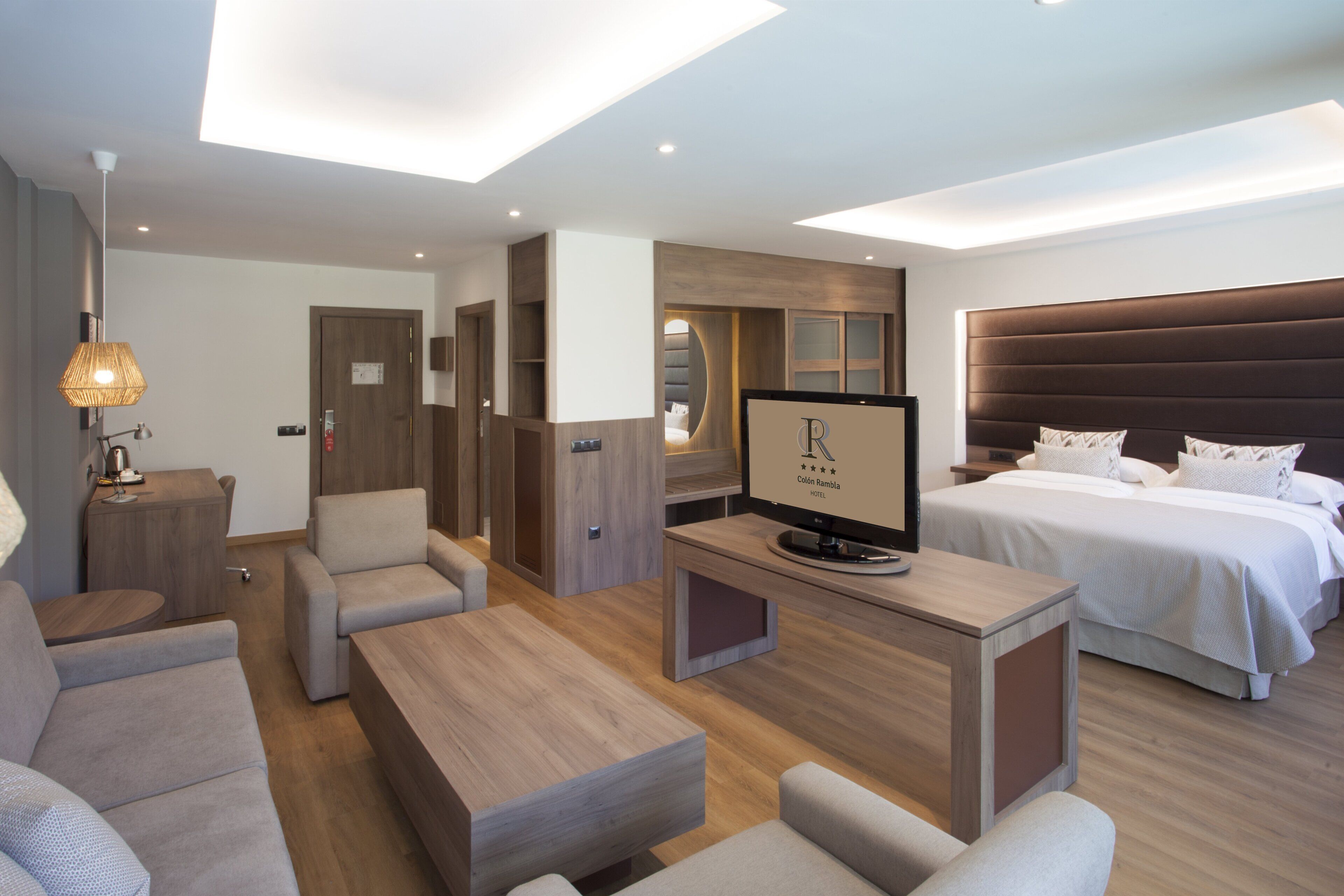 Ein modernes Hotelzimmer mit einem großen Bett, einem Fernseher, einer Couch und einem Schreibtisch.