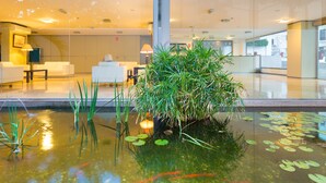 Un vestíbulo con mostrador de recepción, zona de estar y un pequeño estanque interior con nenúfares y peces.