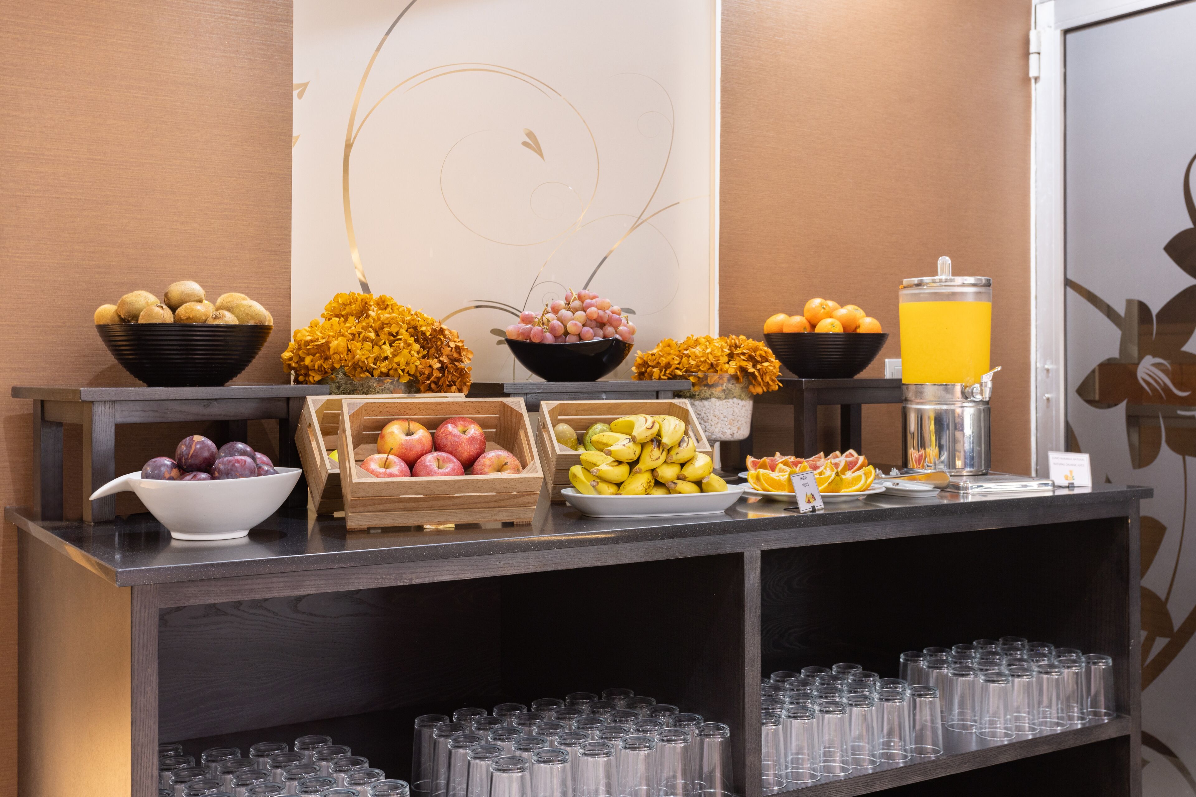 Una mesa de buffet con diversas frutas y un dispensador de jugo.