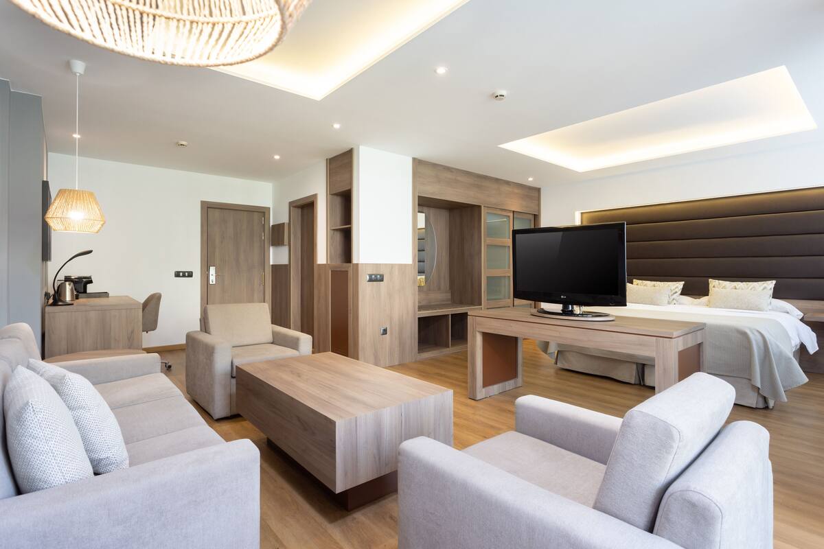 A modern hotel room with a flat-screen TV, a sofa, a coffee table, a desk, and a bed.