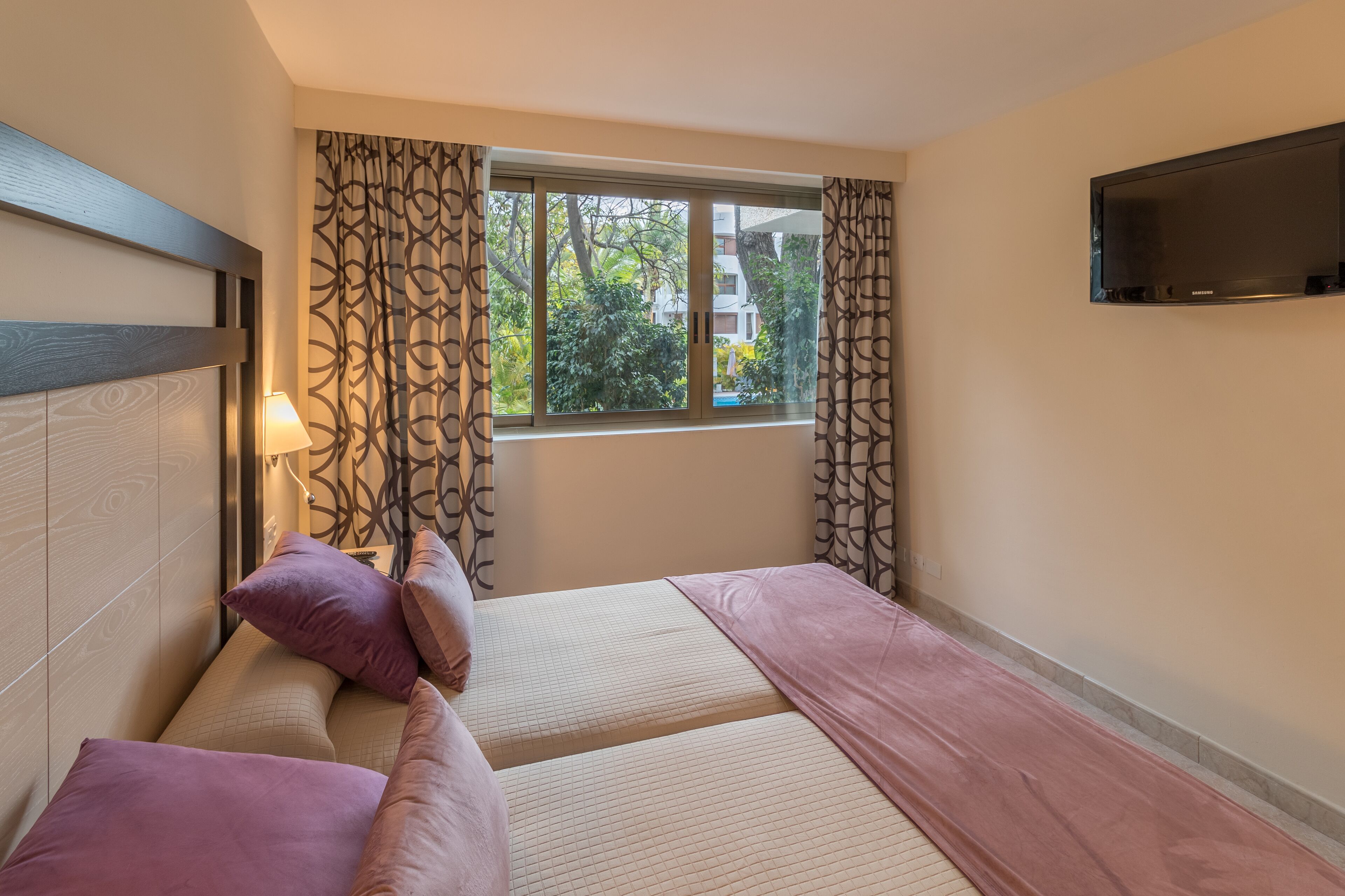Una habitación de hotel con una cama, un televisor montado en la pared y una ventana con cortinas.