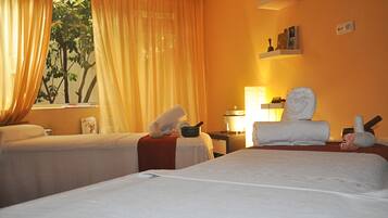 Two single beds with neatly folded towels and a small table in between, set against a simple, clean backdrop.