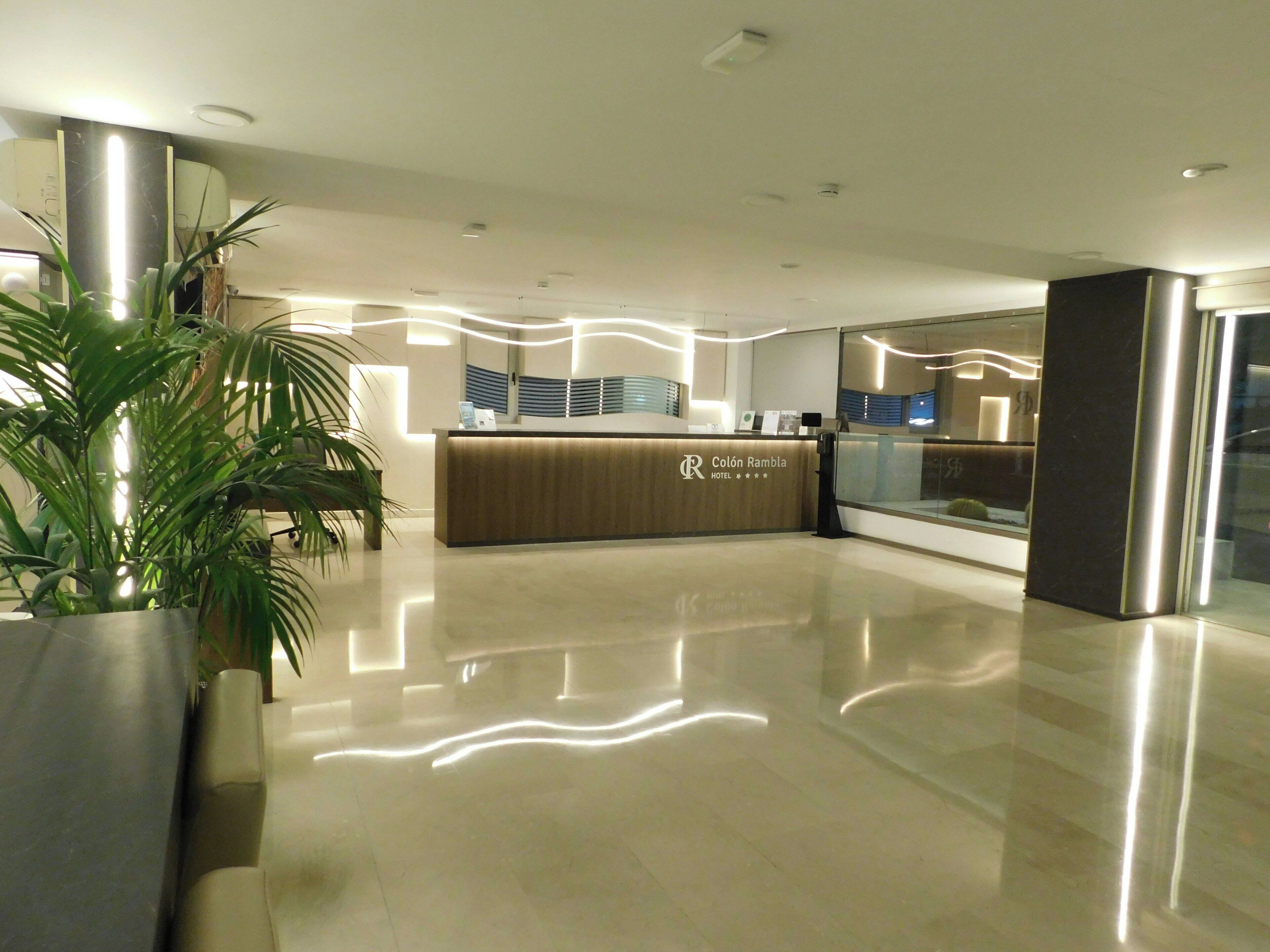 Ein Hotel-Empfangsbereich mit modernem Design, mit einer Rezeption, einer großen Topfpflanze und einer Glastrennwand.