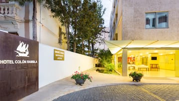 A hotel entrance with a cobblestone path, potted plants, and a sign for 'Hotel Colón Ramblá'.