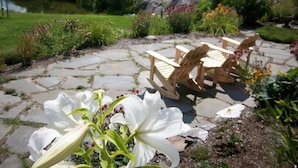 A stone patio with wooden chairs and a table, surrounded by a garden with various plants and flowers. - Coppertoppe Inn and Retreat Center (Hebron)