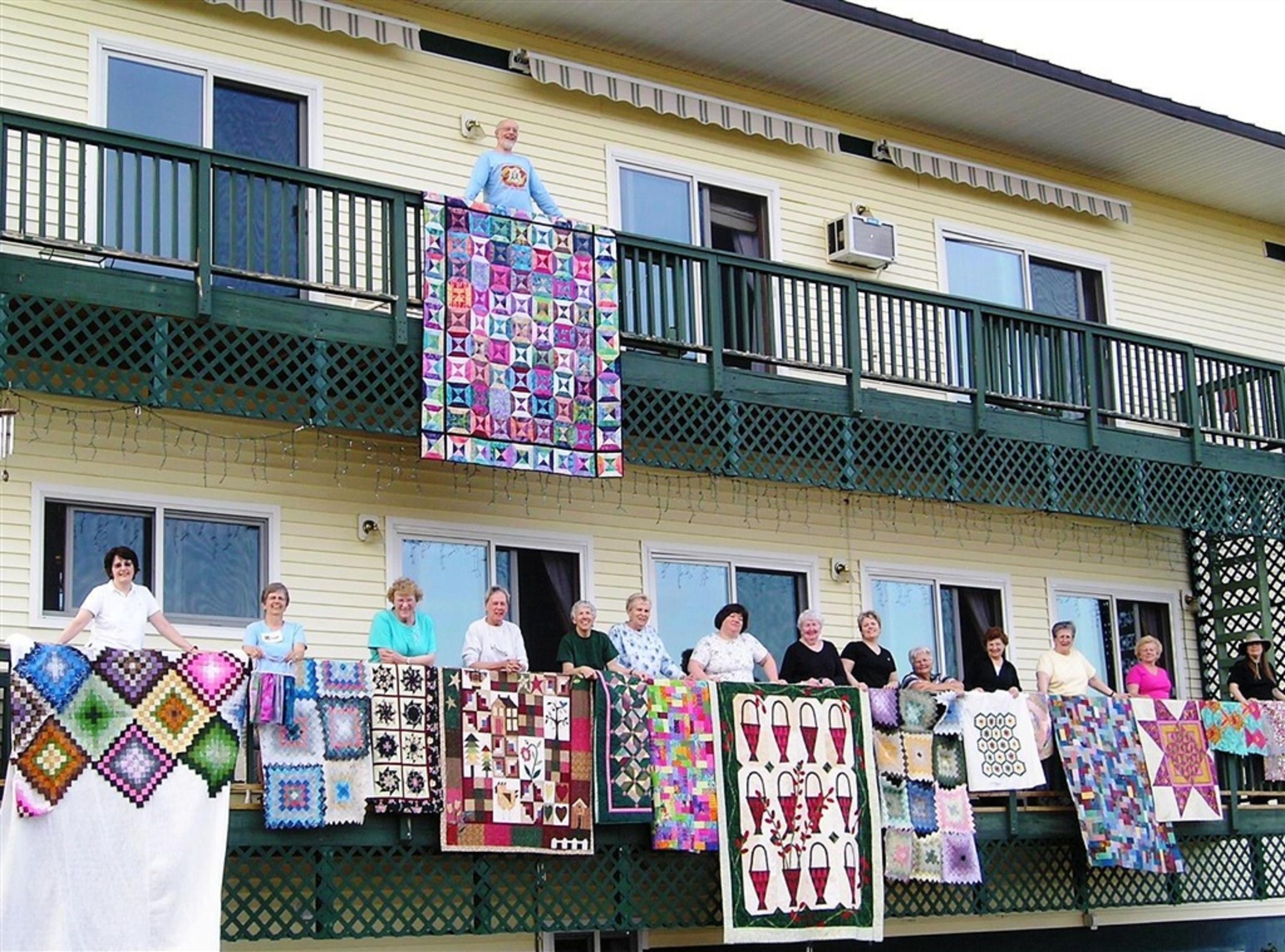 A building with a green balcony and a group of people holding quilts.