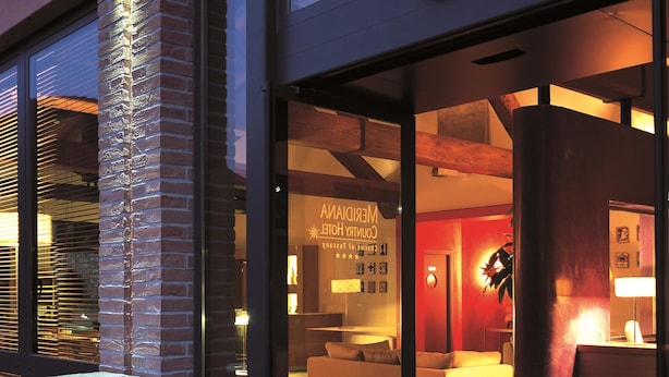 Entrada de hotel con puerta de vidrio, un mostrador de recepción y una zona de estar en el interior.